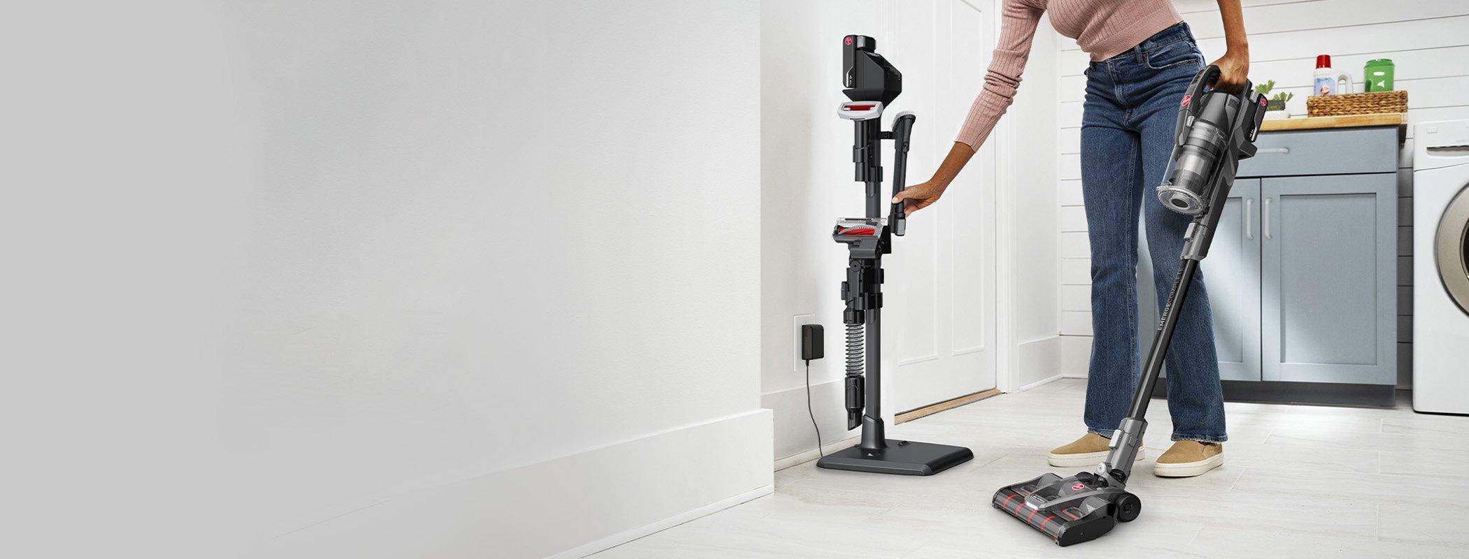 Person placing the Hoover emerge complete vacuum on its standing dock, demonstrating the vacuum's ease of storage and cleaning convenience.  