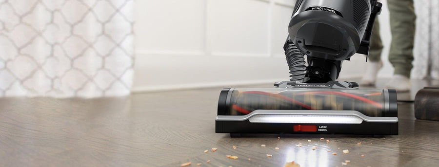 Close up of Hoover vacuum cleaner with tangleguard technology and headlights, effectively cleaning a hard floor with spilled crumbs.