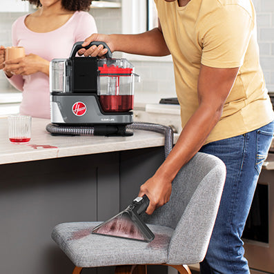 Person using their ONEPWR cleanslate portable spot cleaner to quickly clean a red juice spill from a light grey upholstery kitchen chair