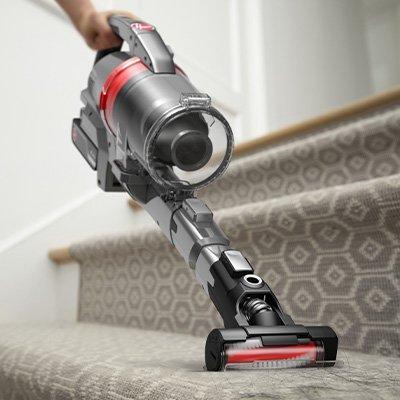 A person using the Hoover emerge pet vacuum cleaner with a motorized tool attachment to clean carpeted stairs, making it ideal for pet owners.