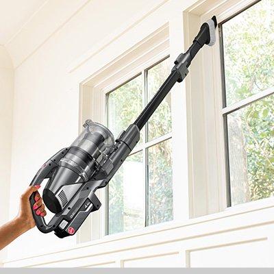 A person using the Hoover 2 in 1 tool attachment to clean high window sills, demonstrating the vacuum's reach and versatility for cleaning hard-to-reach areas.