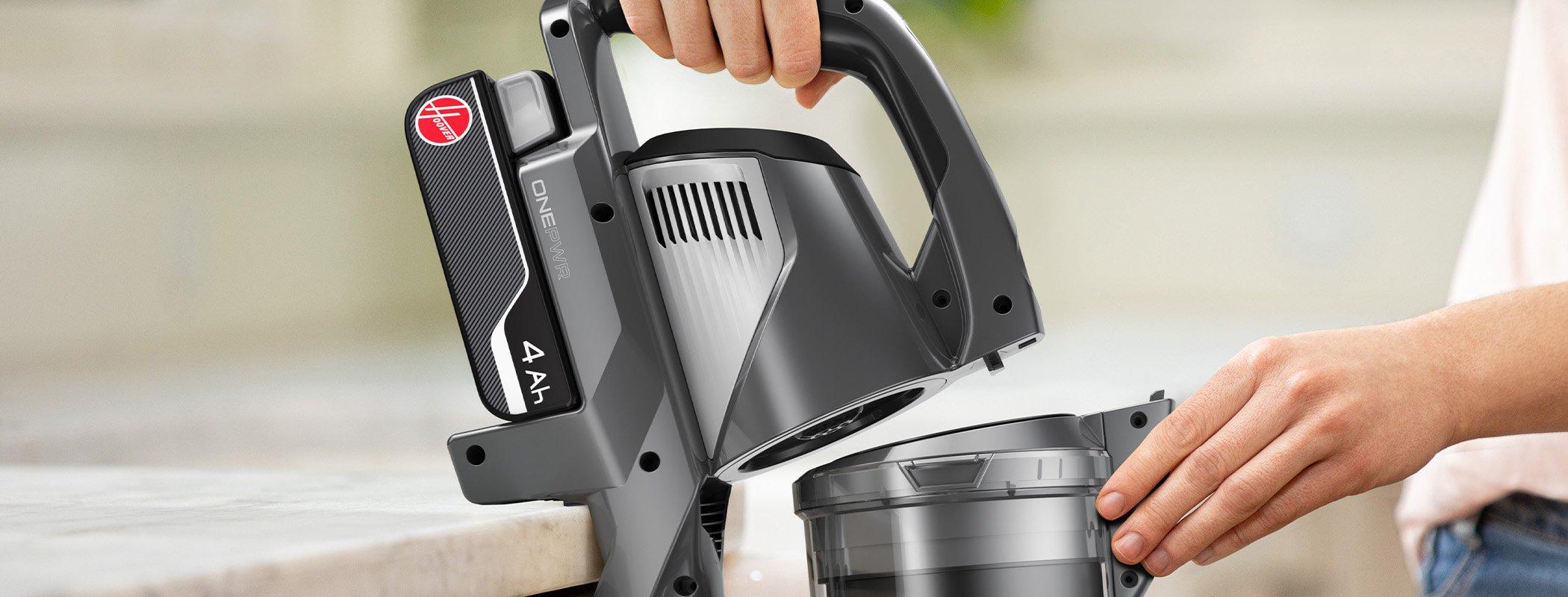 Close up of a person removing the dirt cup from the Hoover emerge complete vacuum, showcasing the vacuum's convenient dirt disposal feature.