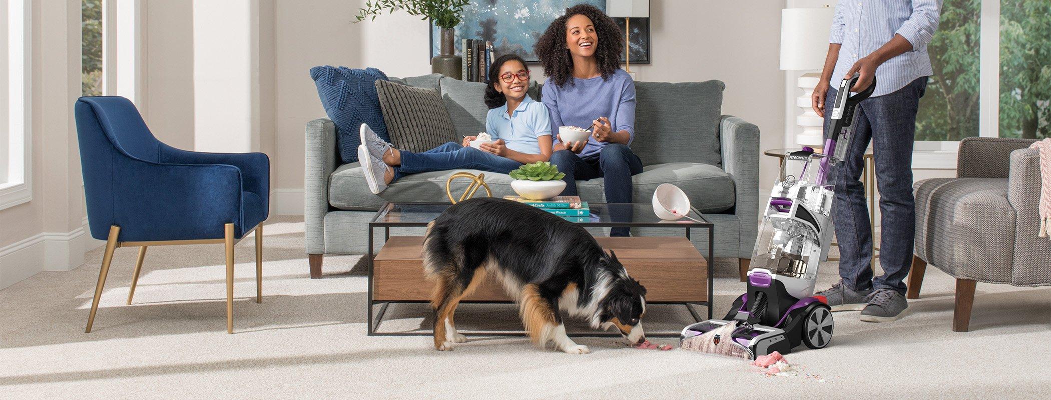 Family and dog shown relaxing in the living room while husband efficiently vacuums the dog's mess