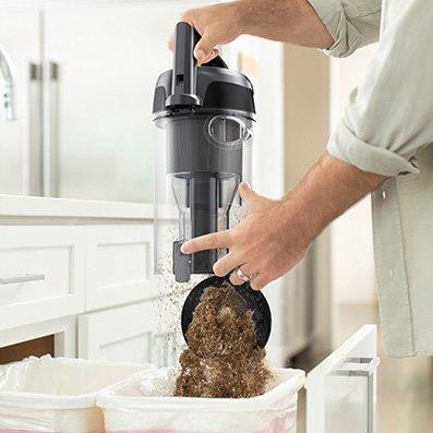 Person emptying the dirt cup of a Hoover vacuum cleaner into a trash bin, highlighting easy dirt disposal.  