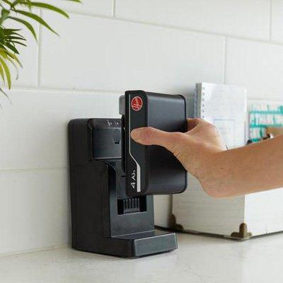 A person inserting a Hoover 4Ah battery into a charging station on a countertop, highlighting the easy-to-charge, removable battery feature of Hoover cordless cleaning products.