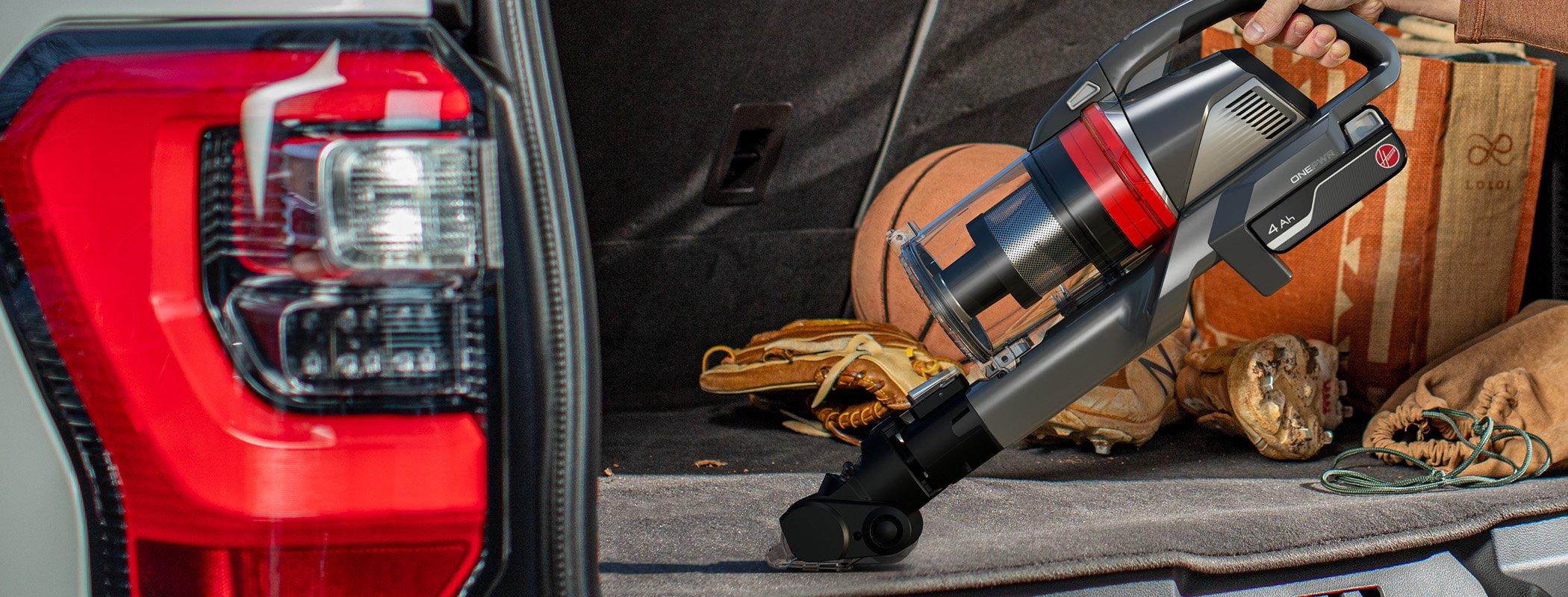 A person using the Hoover emerge pet vacuum cleaner with a motorized tool attachment to clean the trunk of a car, highlighting its portability and effectiveness in cleaning vehicle interiors.