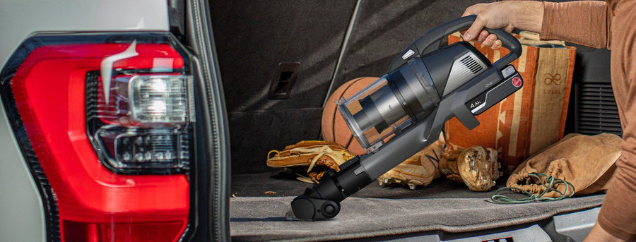 A person using the Hoover emerge pet vacuum cleaner with a motorized tool attachment to clean the trunk of a car, highlighting its portability and effectiveness in cleaning vehicle interiors.