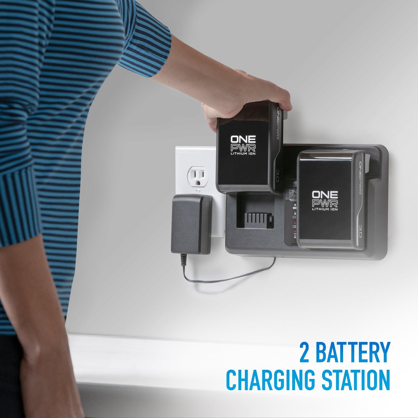 Person placing a Hoover ONEPWR lithium ion battery into a 2-bay battery charging station mounted on a wall, with another battery already charging beside it.