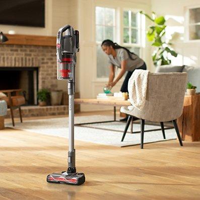 ONEPWR emerge cordless stick standing by itself as woman continues cleaning the living room showcasing its convenient design.  