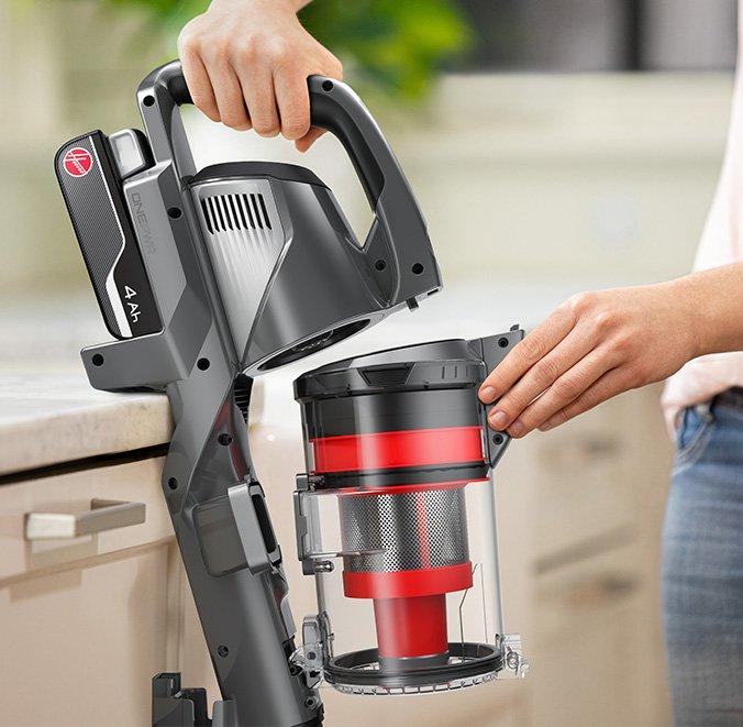 A person holding a Hoover vacuum cleaner while removing the dustbin for emptying.  The vacuum features a 4Ah ONEPWR battery, highlighting the ease of maintenance and convenience of the cordless design. 