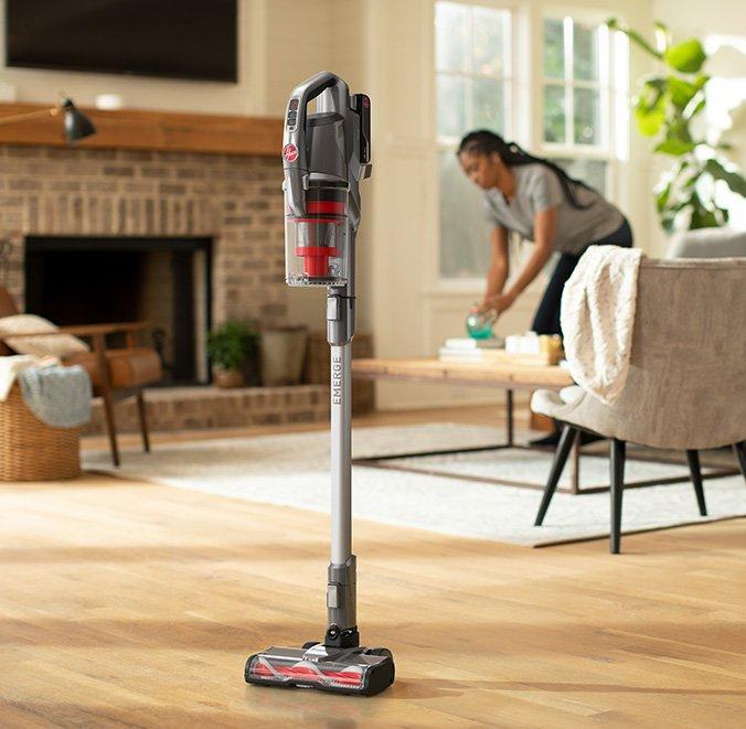 ONEPWR emerge cordless stick standing by itself as woman continues cleaning the living room showcasing its convenient design.  