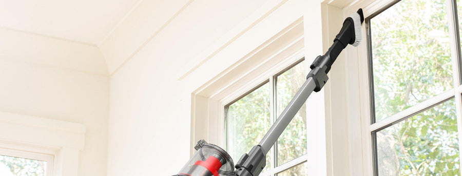 A person using the Hoover 2 in 1 tool attachment to clean high window sills, demonstrating the vacuum's reach and versatility for cleaning hard-to-reach areas.