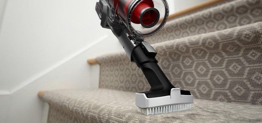 Cordless stick vacuum with stair cleaning attachment in use demonstrating efficient cleaning of carpeted stairs.