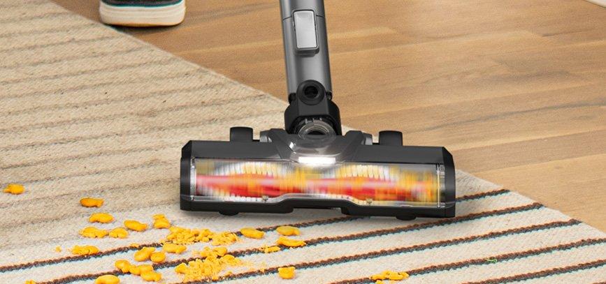 Cordless vacuum cleaner with high performance brush roll is shown in action efficiently picking up goldfish from a light colored area rug.