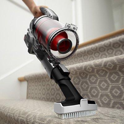 Versatile cordless vacuum cleaner with upholstery tool attachment is being used to effectively remove hair from carpeted stairs.