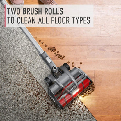 Hoover vacuum cleaner demonstrating its ability to clean both carpet and hard floor types with two brush rolls.  The vacuum is shown picking up pet food from both surfaces, highlighting its versatility 