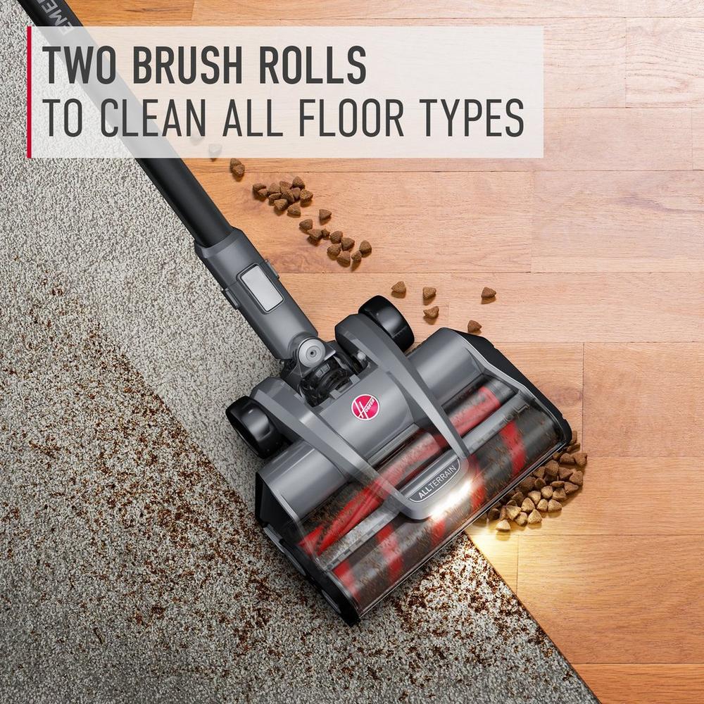 Hoover vacuum cleaner demonstrating its ability to clean both carpet and hard floor types with two brush rolls. The vacuum is shown picking up pet food from both surfaces, highlighting its versatility