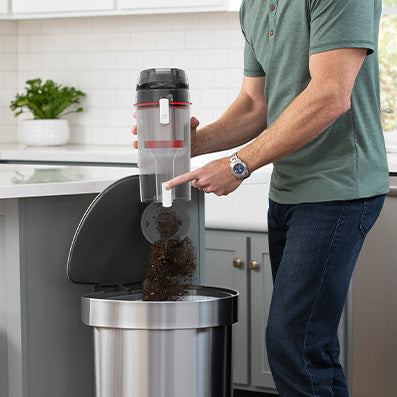 Man shown emptying the dirt cup of his evolve pet elite cordless upright vacuum highlighting its easy clean up