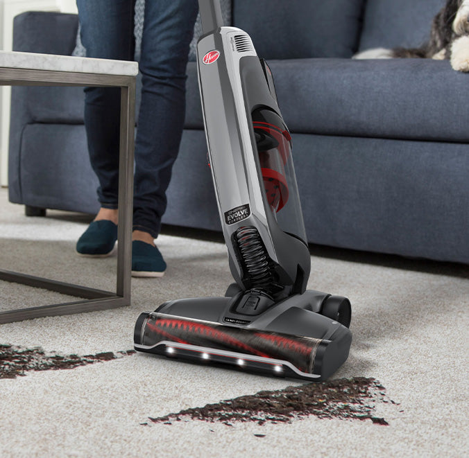 Evolve pet elite is shown bending a corner to effectively vacuum a large dirt mess from white carpet 