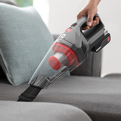 Hoover handheld vacuum cleaner being used to vacuum couch upholstery highlighting its versatility with the 2-in-1 crevice tool and dusting brush.