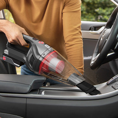 Hoover handheld vacuum being used to clean a car interior demonstrating its versatility and portability.