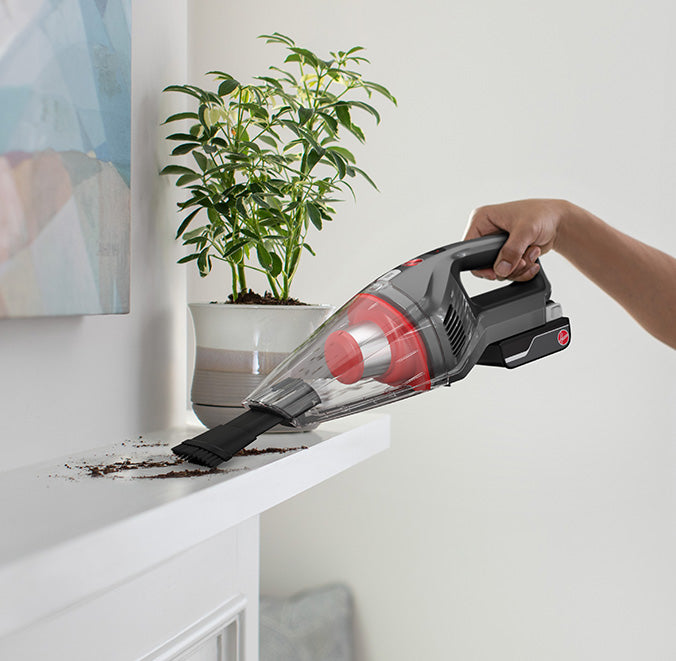 Handheld vacuum is shown in action vacuuming spilled soil from a white shelf.