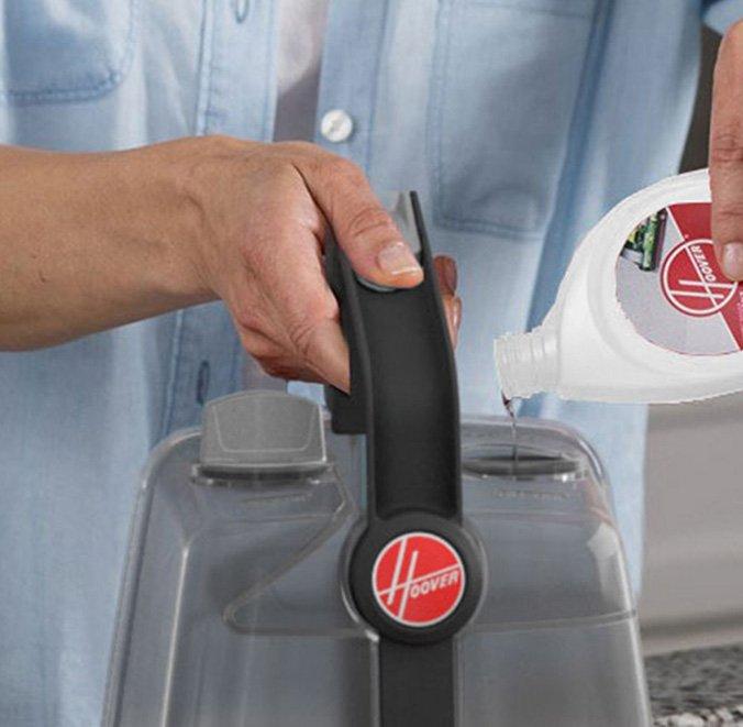 Close up of a person pouring cleaning solution into the Hoover power scrub carpet cleaner's tank, demonstrating the ease of use