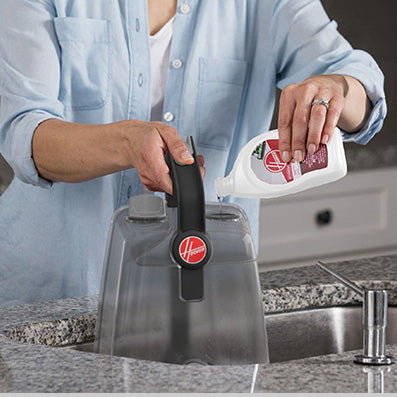 Close up of a person pouring cleaning solution into the Hoover power scrub carpet cleaner's tank, demonstrating the ease of use