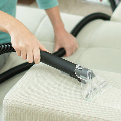 Close up of hand using the Hoover power scrub carpet cleaner to deep clean her couch