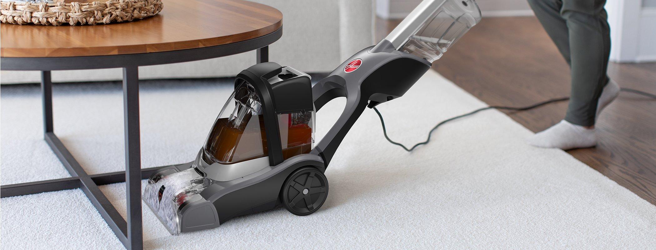 Hoover powerdash pet advanced carpet cleaner being used to clean under a low coffee table highlighting its flexibility to reach tight spaces 