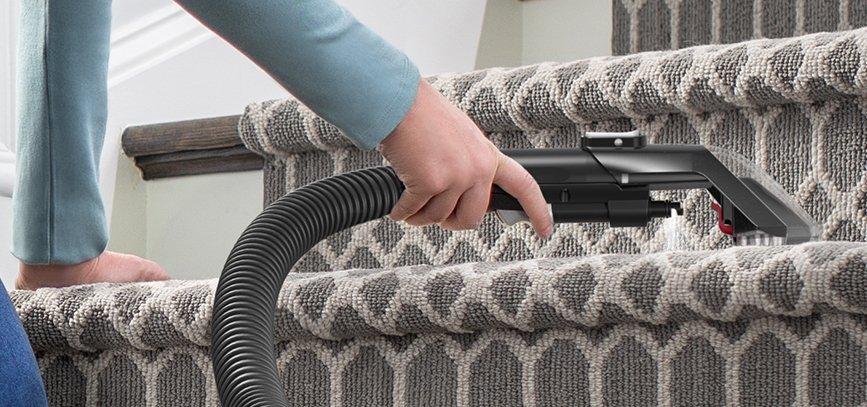 Close up of someone spot cleaning the stairs using the 2 in 1 pet tool attachment to the powerdash pet advanced carpet cleaner