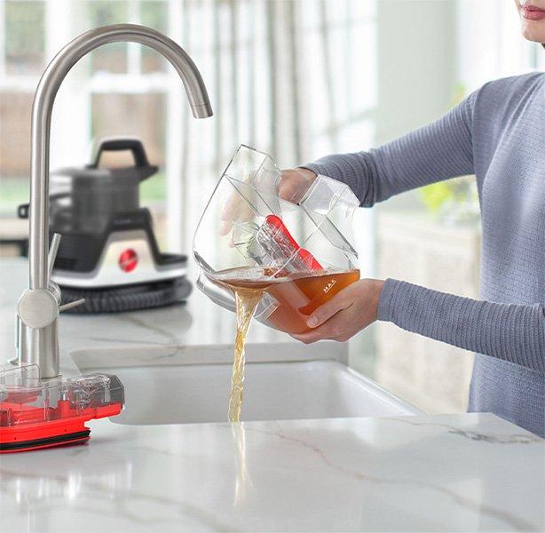 Person emptying the dirty water tank of a Hoover Cleanslate pet spot cleaner highlighting easy maintenance