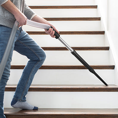 Person vacuuming stairs with a Hoover vacuum cleaner using an extended hose attachment, highlighting its versatility and ease of use on staircases.