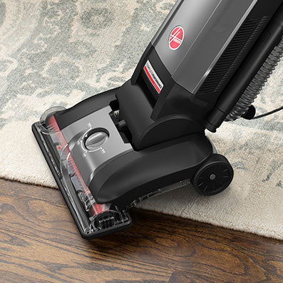 Close up of a Hoover vacuum cleaner on a patterned carpet, demonstrating effective cleaning on a hardwood and carpeted surface.