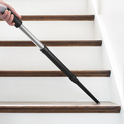 Hand using a vacuum cleaner with an extension wand to clean stairs, showcasing its versatility and effectiveness.  