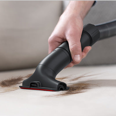 Close up of a hand using the 2-in-1 dusting brush and upholstery tool to vacuum pet hair, demonstrating the effective pet hair removal.  