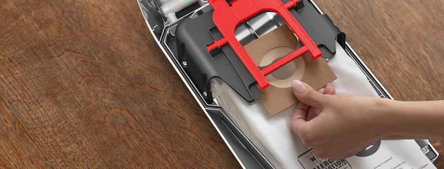 Hand inserting a vacuum cleaner bag into a Hoover upright vacuum, illustrating easy bag replacement.