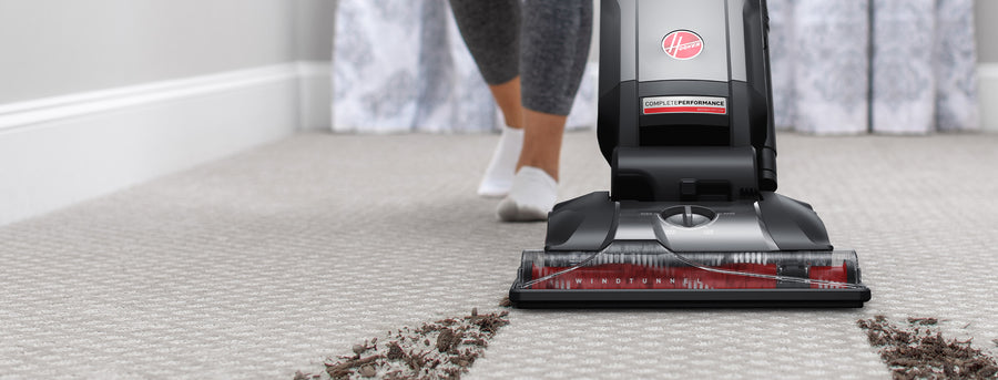 Hoover upright vacuum cleaner in use on a carpet, demonstrating powerful dirt and debris pickup.