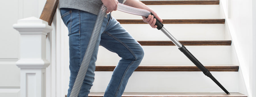 Person vacuuming stairs with a Hoover vacuum cleaner using an extended hose attachment, highlighting its versatility and ease of use on staircases.