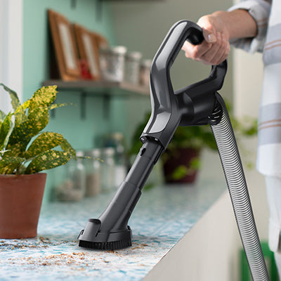 Person using Hoover vacuum cleaner with dusting brush attachment to clean a kitchen counter, showcasing versatile cleaning tool.  