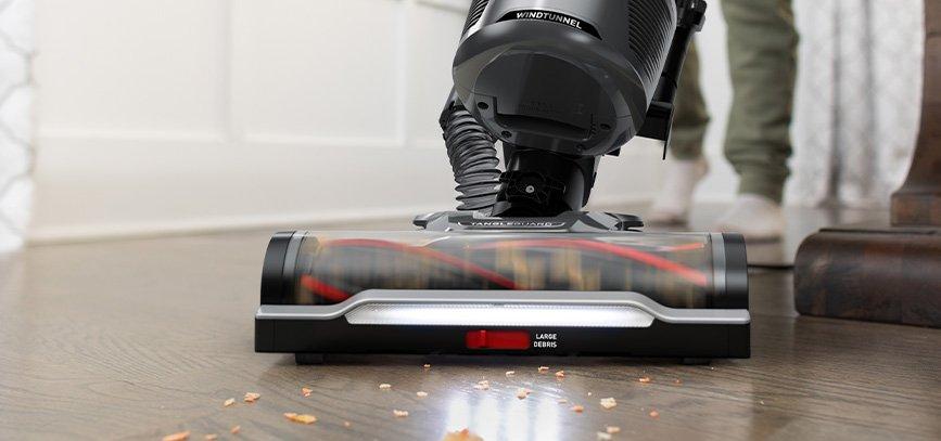 Close up of Hoover vacuum cleaner with tangleguard technology and headlights, effectively cleaning a hard floor with spilled crumbs.