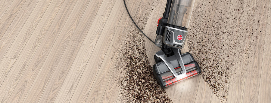 Hoover vacuum cleaner navigating through a large dirt mess on a wooden floor, highlighting its easy maneuverability.