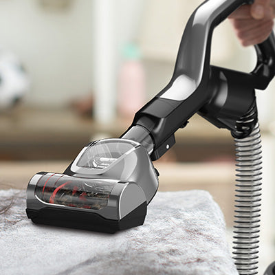 Hoover vacuum cleaner with the hoover turbo tool attachment cleaning a plush gray carpeted cat tree emphasizing its ability to clean textured surfaces effectively.