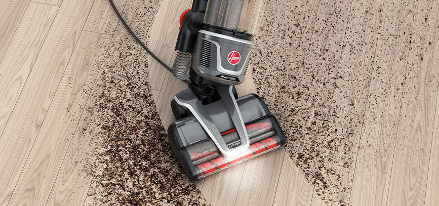 Hoover vacuum cleaner navigating through a large dirt mess on a wooden floor, highlighting its easy maneuverability.