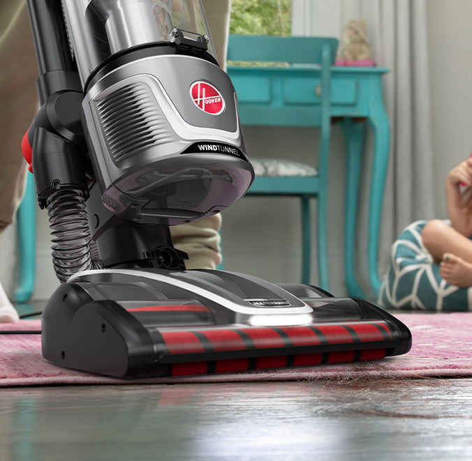 Close up of a Hoover Windtunnel upright vacuum cleaner in use on a pink carpet demonstrating its powerful suction and multi-surface cleaning capabilities.