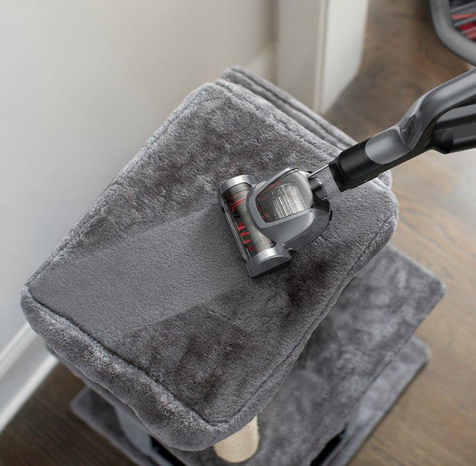 Hoover vacuum cleaner with the hoover turbo tool attachment cleaning a plush gray carpeted cat tree emphasizing its ability to clean textured surfaces effectively.