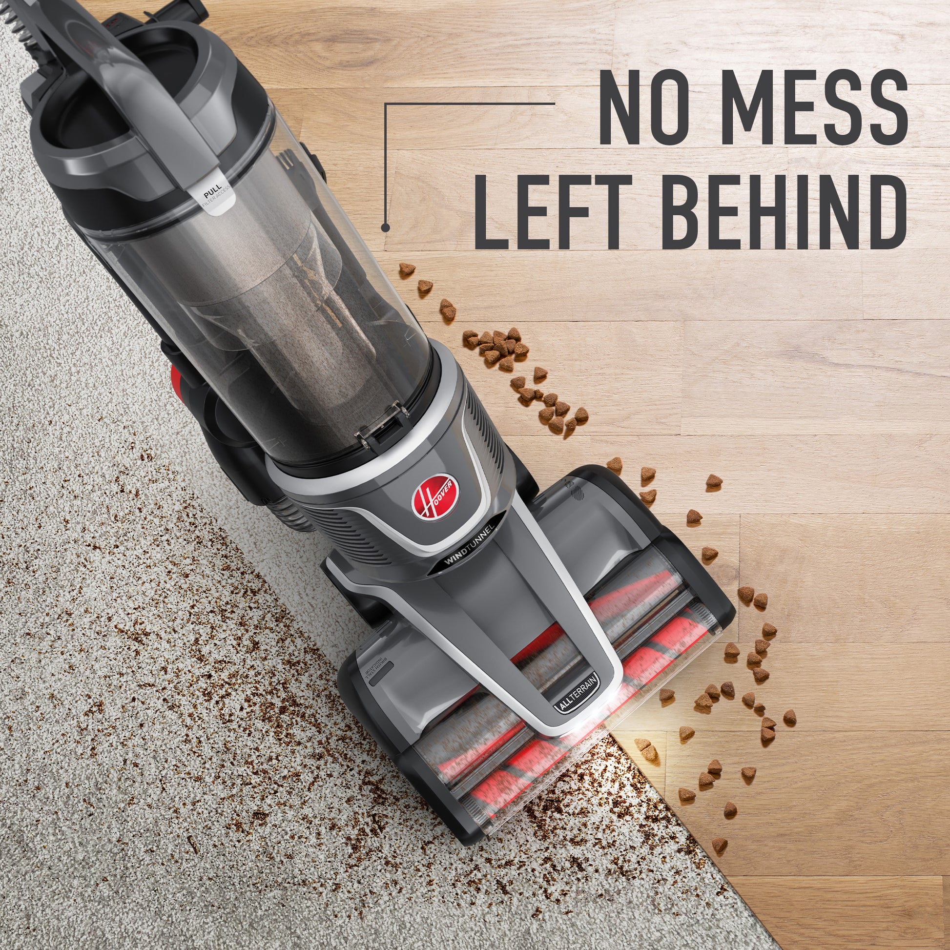 Top down view of a Hoover windtunnel vacuum cleaner seamlessly transitioning from carpet to hardwood floor, effectively picking up scattered pet food and dirt 